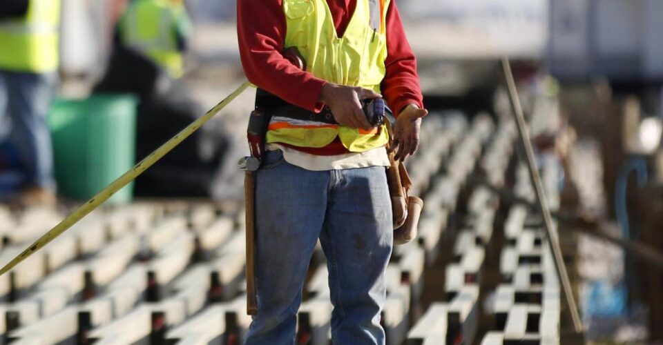 A man in yellow hard hat and safety vest standing on top of a bridge.