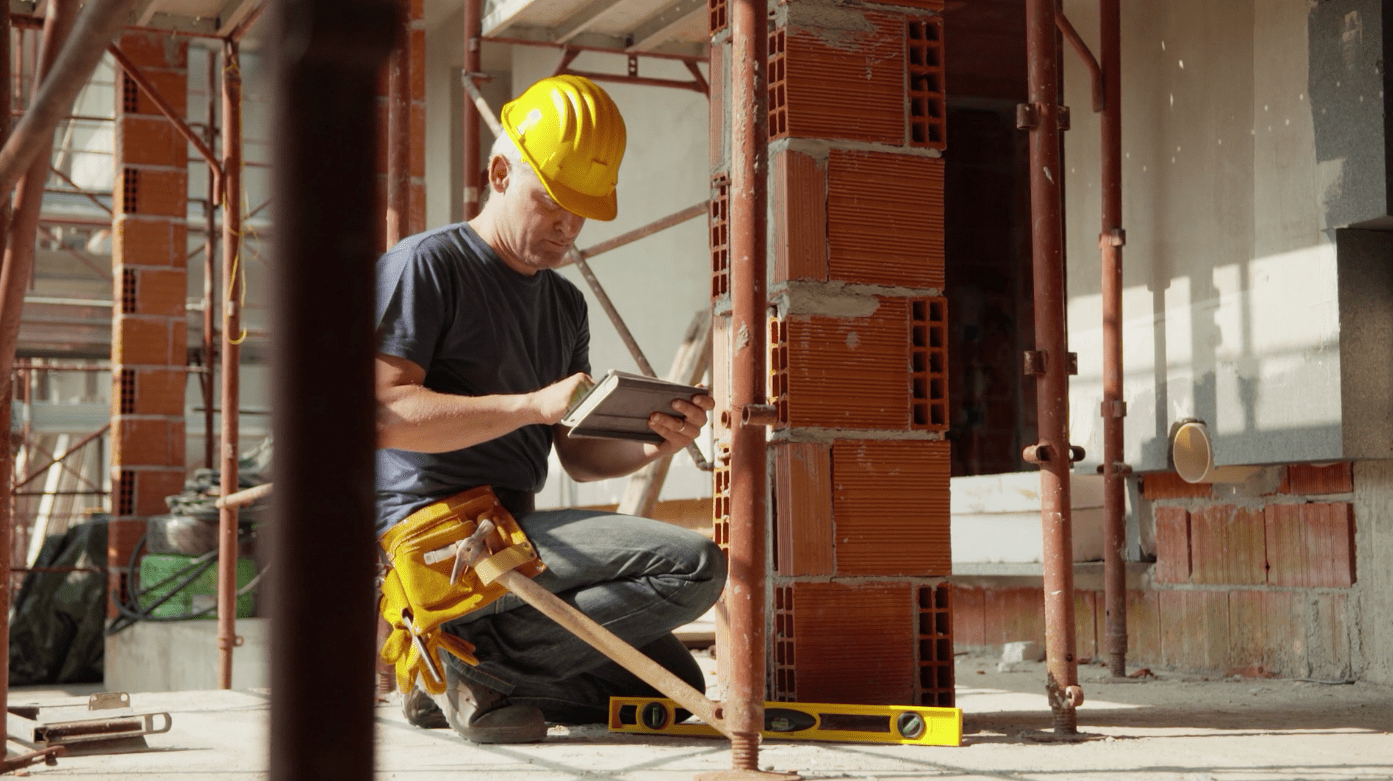 A man in yellow hard hat using his tablet.